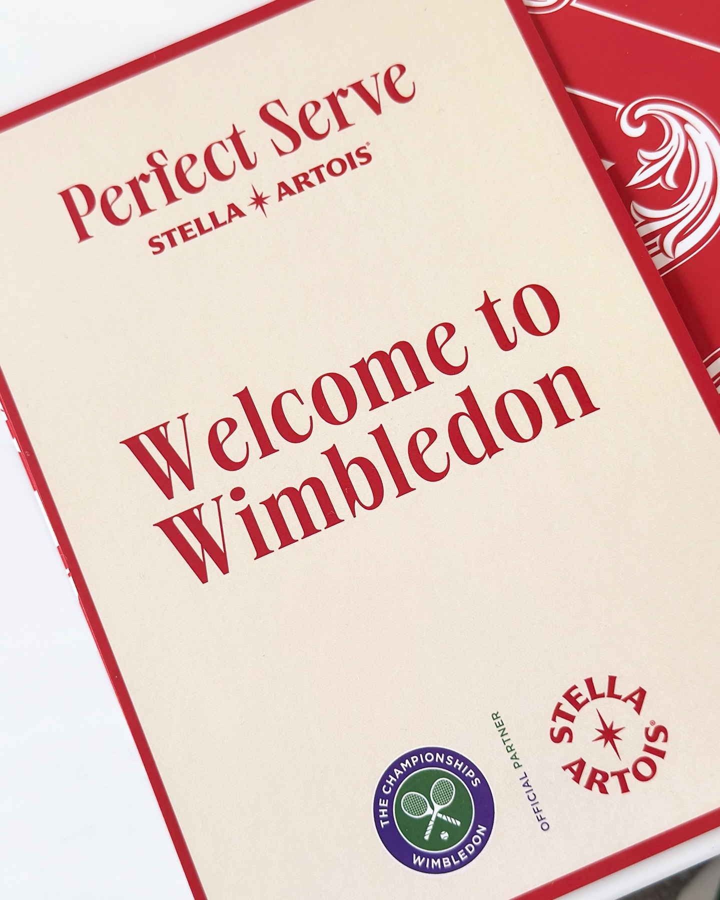스텔라 아르투아 윔블던 퍼펙트 서브 웰컴 카드 'Perfect Serve - Stella Artois'와 'Welcome to Wimbledon'이 적힌 웰컴 카드. Wimbledon 공식 파트너 로고와 스텔라 아르투아 로고가 함께 있다.